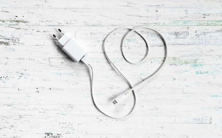 Micro usb charger for handphone white charging cable in form as love shape cable on white wood. Valentine phone charger technology concept.の写真素材