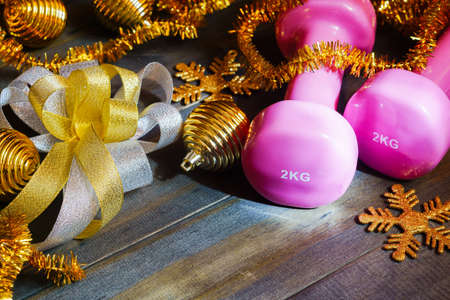 Pink sport dumbbells with Chrismas decoration items and gift bow on wooden background, Merry Christmas and Happy new year wish sport gifts conceptの写真素材