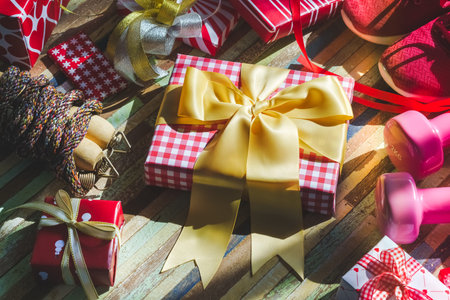 Still life of Christmas sport composition with dumbbells, sport shoes, skipping rope and red gift boxes with bow on wood background.  Merry Christmas and Happy new year and any holidy present boxes for healthy and active lifestyle with sport.の写真素材