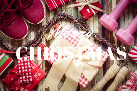 Flat lay of Merry Christmas and Happy new year and any holidy present boxes for healthy and active lifestyle concepts. Composition with dumbbells, sport shoes, skipping rope and red gift boxes with bow on wood background.の写真素材
