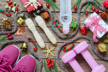 Fitness, healthy and active lifestyles greeting card concept, dumbbells, sport shoes, skipping rope or jump rope with Christmas decoration on wood background. Exercise, Fitness and Working Out Merry Christmas and Happy new year concept.の写真素材