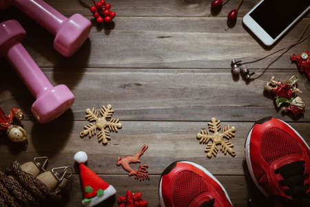 Fitness, healthy and active lifestyles love concept, dumbbells, sport shoes, skipping rope or jump rope and smart phone with Christmas decoration items on wood background. Working Out Merry Christmas concept.の写真素材