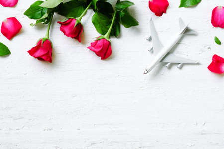 Flat lay of white blank model of passenger plane with roses over white rustic wooden background. Top view with copy space.  Travelling on Valentine's day background concept.の写真素材