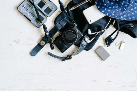 Flat lay top view of female photogarpher summer holiday travel backpack stuffs with  digital camera, sd-card, battery, hat, thumb drive, mobile phone in the black bag on the grunge white wooden background.の写真素材