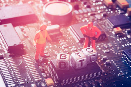 Bitcoin BTC Cryptocurrency mining concept. Miniature virtual miner engineer working on the motherboard for mining the Bitcoin cryptocurrency.の写真素材