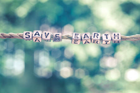 Save Earth word hanging by rope with beautiful green nature bokeh background with vintage retro tone.の写真素材