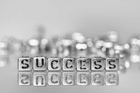Success word written on grunge silver cube  with black and white bokeh backgroundの写真素材