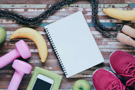 Fitness and healthy active lifestyle dieting background concept. Dumbbell, jump ropes, apples, bananas and blank notebook on wood background. Top view with copy space.の写真素材