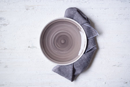 Empty earth tone plate with napkin on rustic grunge white wooden background.  View from above with...