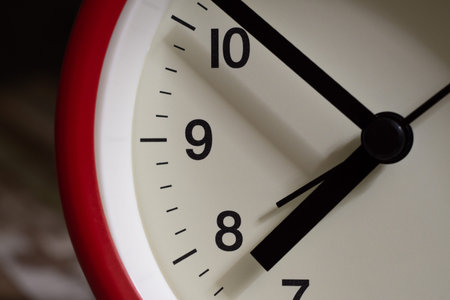 Red alarm clock close up. It's showing ten minutes to eight o'clock before alarm at eight.