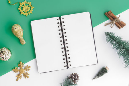 Creative flat lay of craft and blank notebook mock up with christmas ornaments on green and white...