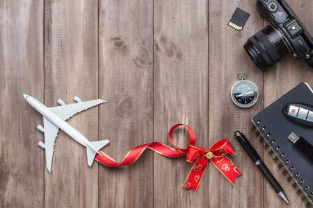 Travel holiday concept. White model of passenger plane with heart bows, camera, sd card, USB drive, compass and notebook on rusty wood background, top view with copy space. Special for travel holiday on New years or Valentines.の写真素材