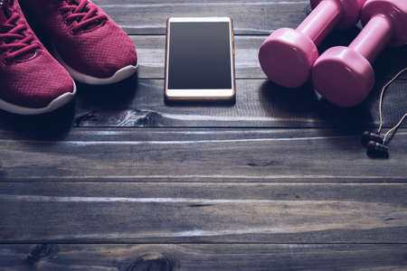 Fitness, healthy and active lifestyles Concept, dumbbells, sport shoes,  smartphone with earphone on wood background. copy space for text.の写真素材