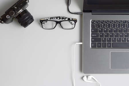 Top view office table concept with camera, laptop notebook, glasses and earphone smartphone on grey table background. Flat lay with copy space.の写真素材