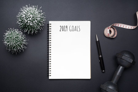 2019 new years resolutions sport flat lay composition. Black dumbbells, measurement tape, blank...
