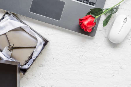 Buying gift via Internet Shopping on Valentines day concept. Laptop with new purse in box and rose flower on white wood background. Top view, Flat lay with copy space.の写真素材