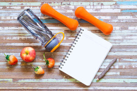 Flat lay of apple, strawberry, dumbbells, blank space notebook, and bottle of water on rusty white background. Top view with copy space on notebook for your text. Active healthy lifestyle background concept.の写真素材