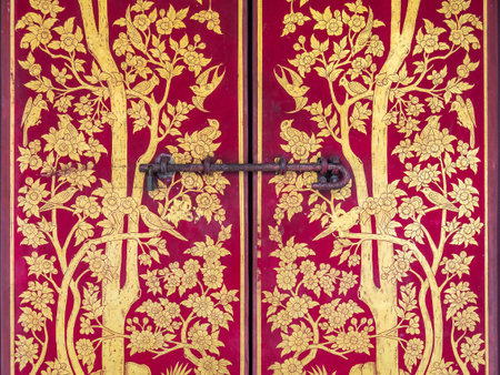 Detail of beautiful traditional Thai style gold paintings with birds and trees on a red wood door at...