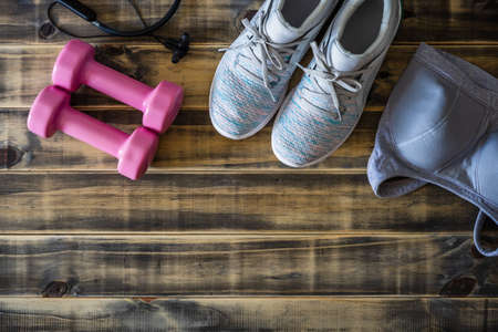 Female fitness and healthy active lifestyle workout background concept.  Training shoes, pink dumbbell, sport bra, and headphones on wooden backdrop. Flat lay top view with copy space.の写真素材