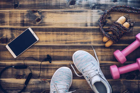 Fitness and healthy active lifestyle background concept.  Training sneakers, dumbbells, jump rope,  smart phone and headphones on wooden backdrop. Top view with space for your advertisement text.の写真素材