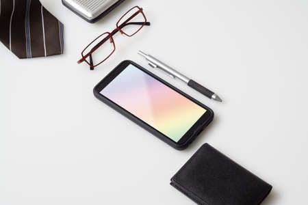Mobile phone mockup with gentlemen's accessories, glasses, wallet, pen and necktie with copy space on white color background. Top view Office desktop with accessories, Desktop with business objects.の写真素材