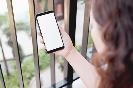 Mockup image of a woman using smart phone with blank white screen at home and garden nature on the...