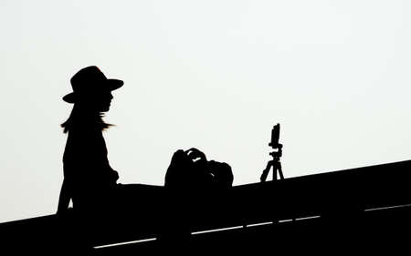 Silhouettes young woman with smartphone on tripod taking selfies on white backgroundの写真素材