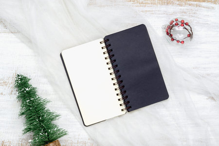 Top view of blank notebook on nest fabric and white wood  background with xmas decorations. Mockup...