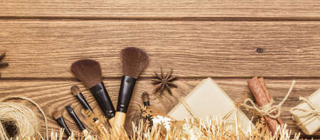 Makeup in christmas time web banner. Makeup Brush and Hand crafted Christmas gift box on wood background. Giving makeup as a present for Christmas, New year or other anniversary.の写真素材