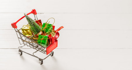 Shopping cart with christmas tree and miniature gift boxes on white wooden table. Christmas and New Year shopping time web banner background concept.の写真素材
