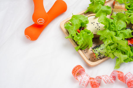 Fitness, fresh healthy salad, diet and active lifestyles, weight loss and detox concept. Diet food, tape measure, dumbbells on white background, top view with copy spaceの写真素材