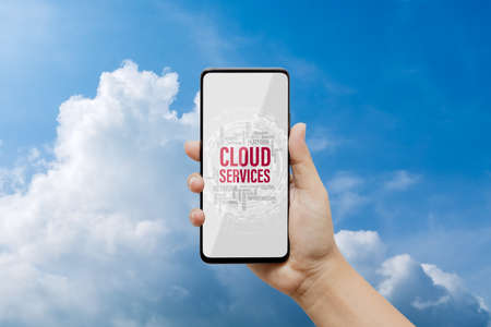 Cloud computing technology background concept. Mockup mobile phone with Cloud Services in word tag on smartphone screen with blue sky and white clouds background.の写真素材
