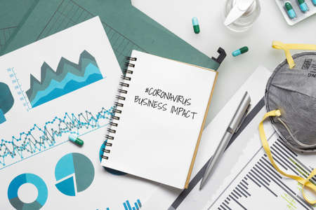 COVID-19 or Corona virus Business IMPACT background concept. Mockup Notebook for Covid 19 business impact anlysis with busines graphs sheets, N95 facial masks and Alcohol Hand Sanitizer gel with on working office desk.の写真素材
