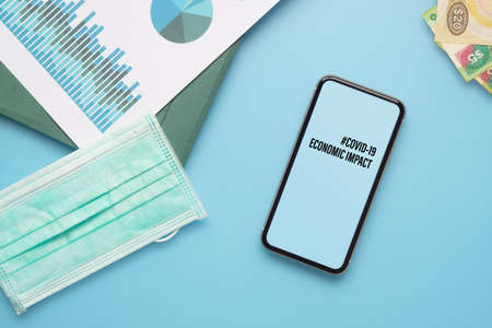Coronavirus Covid-19 pandemic outbreak economic impact background concept. Mockup mobile phone with computer keyboard, business charts, facemask and hand sanitizer hel on working table for covid 19  business financial risk.の写真素材
