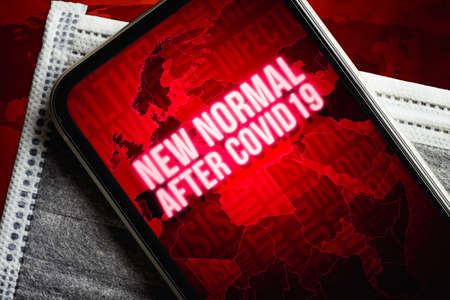 A smartphone with new normal after covid19 message with world map on the medical face mask on grunge redの写真素材