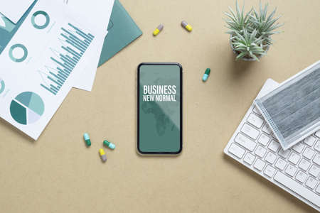 Business New normal after Covid 19 Outbreak background concept. Mockup mobile phone for Covid19 business New Normal with facial mask, medicine tablet, financial chart on working table.の写真素材
