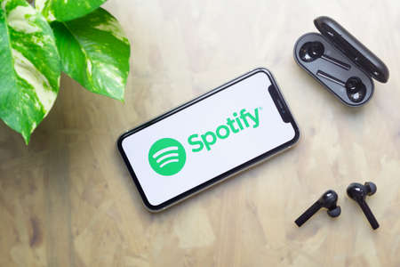 Bangkok, Thailand - July 3, 2020: Apple Iphone 11  with Spotify logo on display, bluetooth headphones with case, green plant on working table background. Flat lay Top viewのeditorial素材