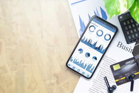 Top view of office desk table with business reports graph chart on mockup smartphone on businessman...