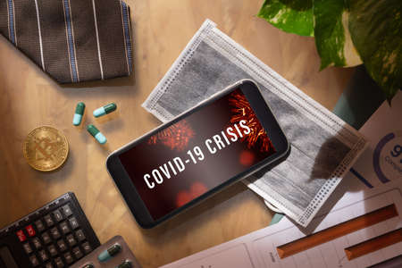 Coronavirus or Covid-19 business and econamic crisis background concept. Mockup mobile phone with facial masks and medical tablets on businessman's office wood desk table.の写真素材