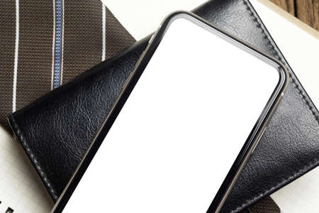 Mockup Blank white screen mobile phone. Flat lay top view of empty screen smartphone over notebook and businessman's necktie on working office deskの写真素材