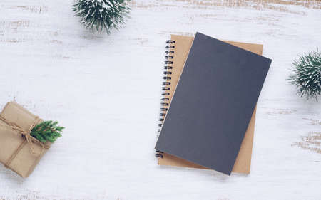 Mockup blank black book cover with Christmas gift box and Christmas tree model decor on white wooden table background. Flat lay, Top view with copy spaceの写真素材