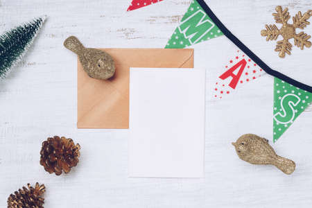 Blank Christmas Card and gold brown envelope with Christmas decorations. Xmas tree models and ornaments, top view. Holiday party workspace mock up, postcard with copy space.の写真素材