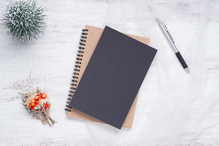 Mockup blank black book cover with pen, Christmas ornaments decor on white grunge wooden table background. Flat lay, Top view with copy spaceの写真素材