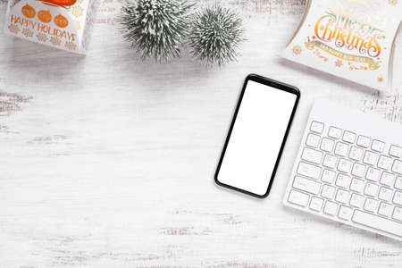 Mockup smartphone with blank white screen, new year gift box with Xmas pine tree model, christmas ornaments on grunge white wood background, top view, place for your artworkの写真素材