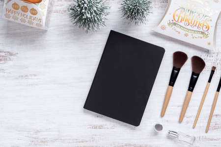 Mockup beauty Christmas New Year concept. Mock up blank empty space black cover book with makeup cosmetic and Christmas decoration ornaments on grunge white desk table background, top view.の写真素材