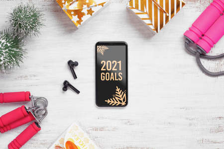 2021 New Year resolutions  healthy goals background concept. 2021 Goals text on mobile phone on table with jump rope, wireless earphone,  and Christmas ornaments. Mock up smartphone.の写真素材