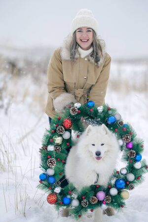 A young girl walks in winter with a white Samoyed dog in a snowy meadow in the forest.の写真素材