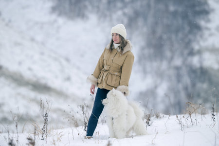 A young girl walks in winter with a white Samoyed dog in a snowy meadow in the forest.
