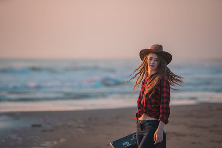 A young slender long-haired brunette in a red dress walks barefoot on a tropical beach with a...