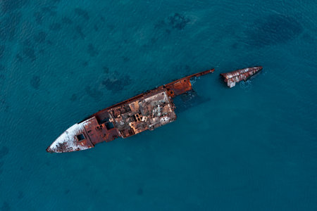 A sunken shipwreck on the reef, a dry cargo ship lies on the bottom of the port side, slowly rusts and collapses. A large seagoing dry-cargo vessel washed ashore in a strong gale, breaking it in two, covered in red rust.の写真素材